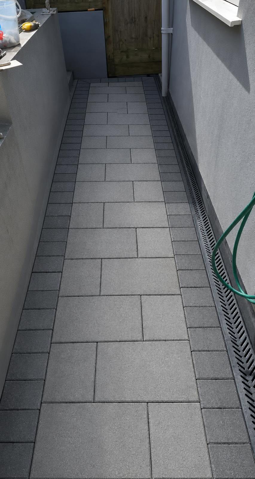 After: the same side passage finished with grey paving slabs laid neatly between block borders and a drainage channel
